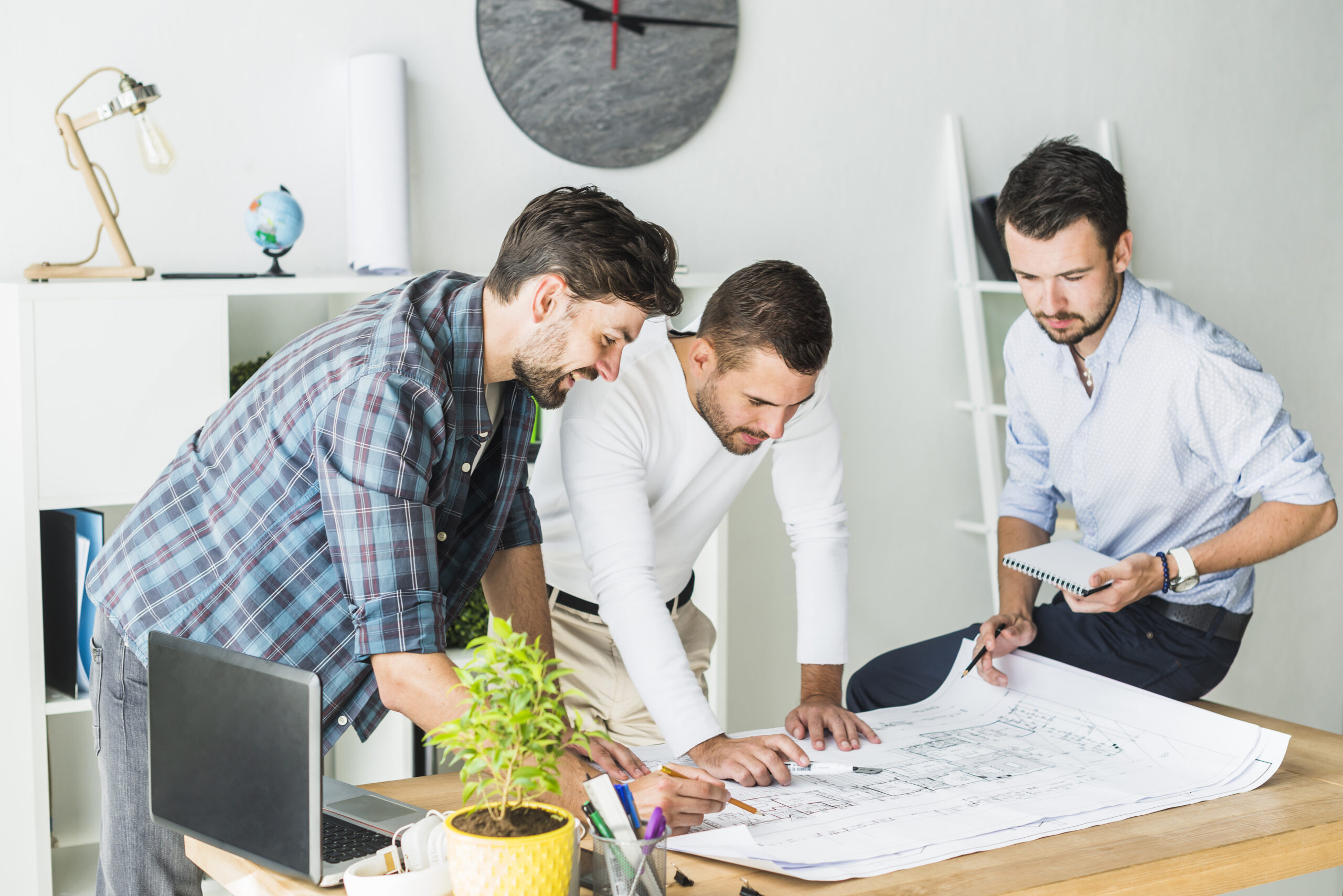Three male architects are reviewing a large blueprint together in a modern office.